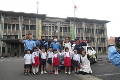 警察署を背にパトカーと警察官と記念撮影をしている様子